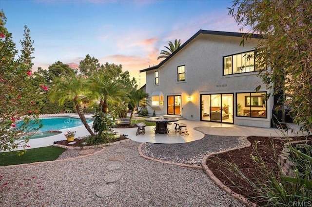 back house at dusk featuring an outdoor fire pit, a patio area, and a swimming pool with hot tub