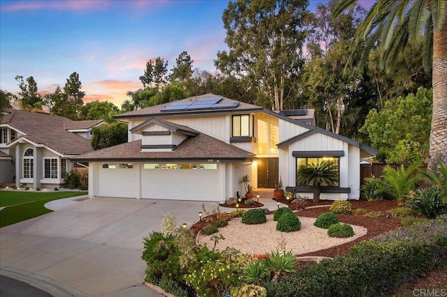 view of front of home with a garage, concrete driveway, roof with shingles, and solar panels