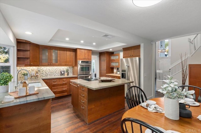 kitchen with stainless steel appliances, a sink, visible vents, brown cabinetry, and a raised ceiling