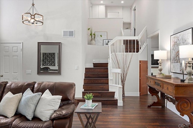 living area with a chandelier, wood finished floors, a towering ceiling, visible vents, and stairway