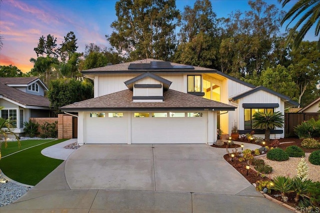 view of front of house featuring an attached garage, concrete driveway, solar panels, and fence