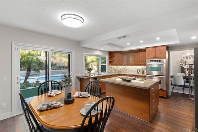 kitchen featuring stainless steel double oven, visible vents, a center island, brown cabinetry, and a raised ceiling