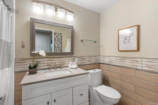 full bathroom with a wainscoted wall, tile walls, a textured wall, toilet, and vanity