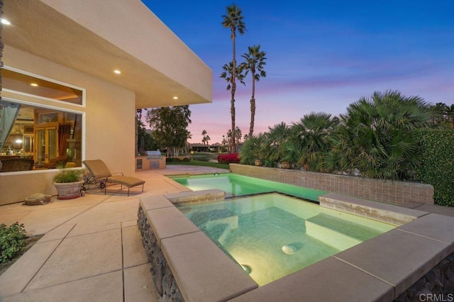 pool at dusk with an in ground hot tub and a patio