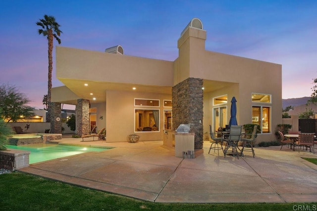 rear view of house featuring a patio area, a pool with connected hot tub, and stucco siding