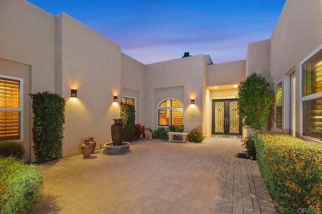 exterior entry at dusk featuring a patio, french doors, and stucco siding