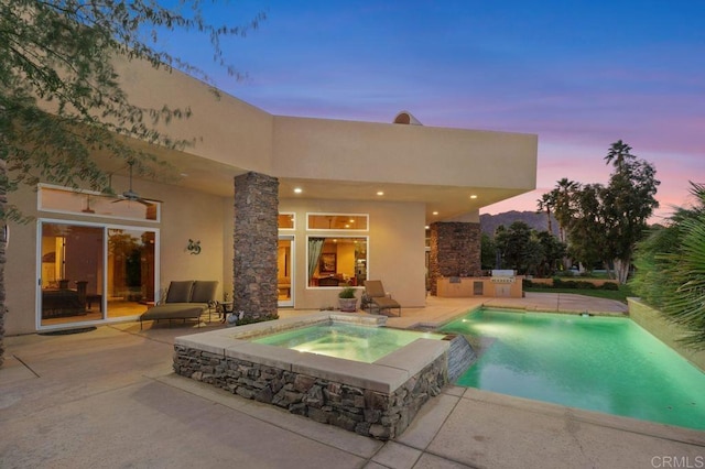 view of pool featuring a patio area, a pool with connected hot tub, a ceiling fan, and exterior kitchen