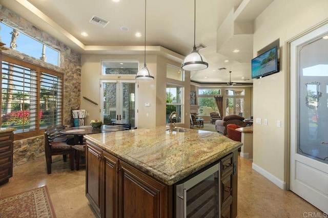 kitchen featuring visible vents, wine cooler, light stone counters, open floor plan, and a sink