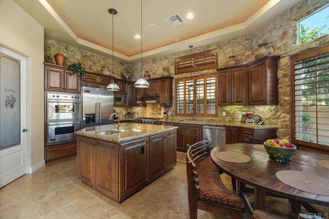 kitchen featuring built in appliances, under cabinet range hood, a sink, visible vents, and a raised ceiling