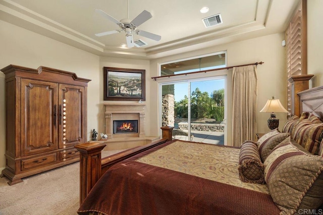 bedroom with a warm lit fireplace, access to outside, visible vents, and a raised ceiling