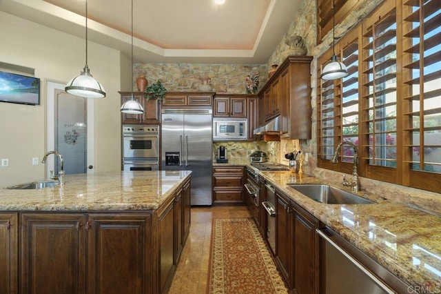 kitchen featuring built in appliances, a raised ceiling, light stone counters, and a sink