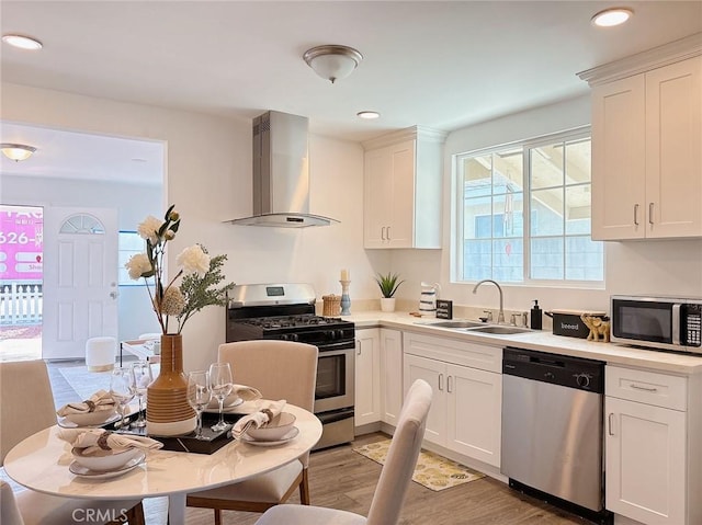 kitchen featuring wall chimney range hood, stainless steel appliances, and white cabinetry