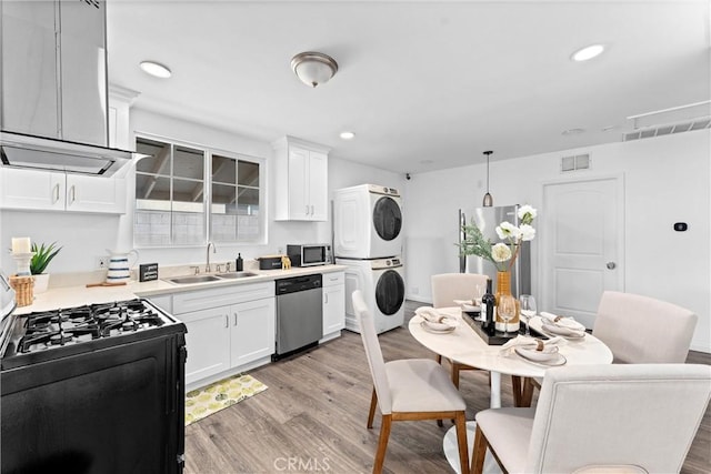 kitchen with dishwasher, sink, hanging light fixtures, stacked washer and clothes dryer, and range with gas stovetop