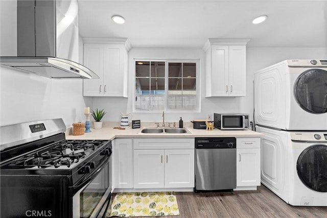 kitchen with appliances with stainless steel finishes, wall chimney exhaust hood, white cabinetry, sink, and stacked washer and clothes dryer