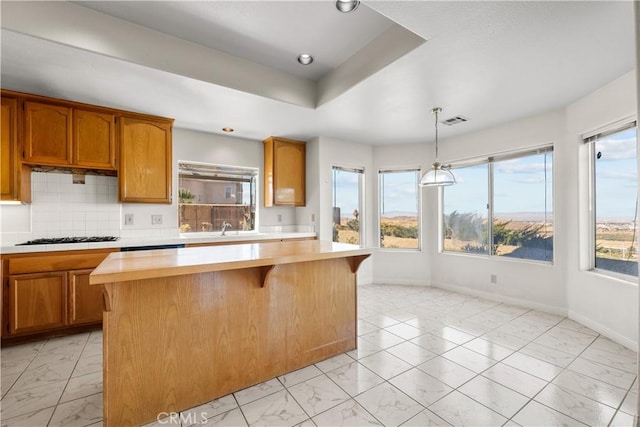 kitchen featuring a center island, decorative backsplash, sink, hanging light fixtures, and gas stovetop