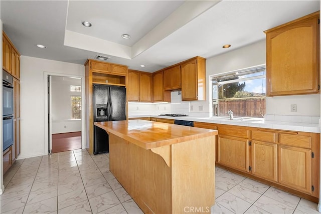 kitchen with wooden counters, a tray ceiling, a kitchen island, black appliances, and sink