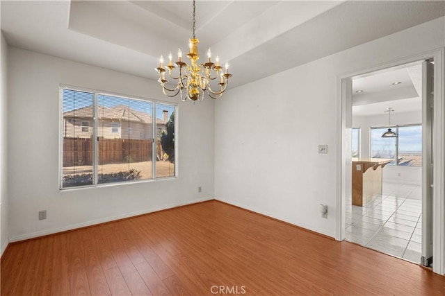 unfurnished room featuring hardwood / wood-style flooring, plenty of natural light, a raised ceiling, and a notable chandelier