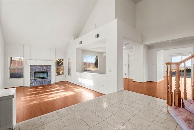 unfurnished living room with a tiled fireplace, an inviting chandelier, and a high ceiling