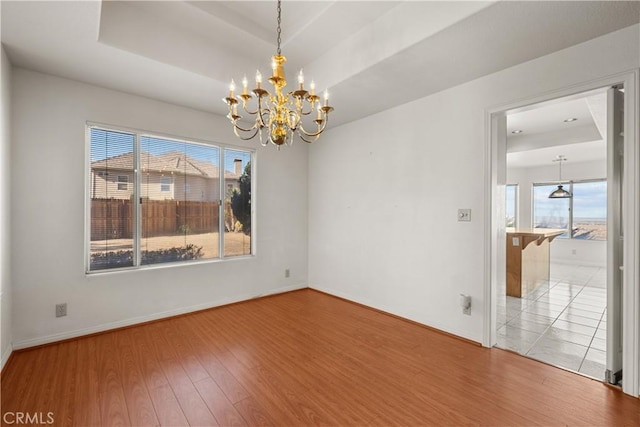 unfurnished room with plenty of natural light, a chandelier, wood-type flooring, and a raised ceiling