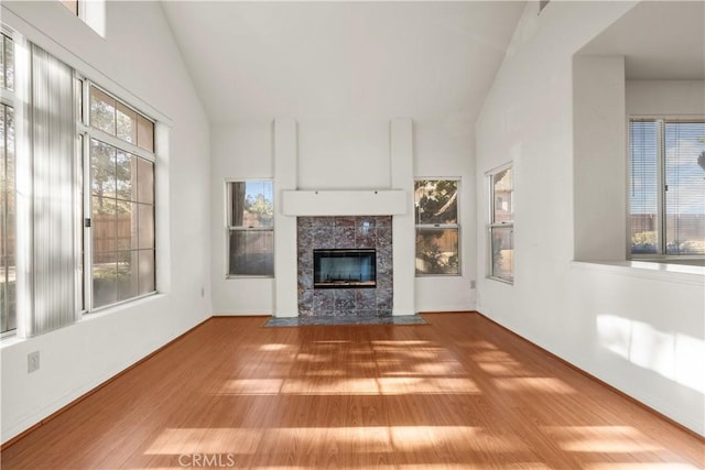 unfurnished living room featuring high vaulted ceiling, a tile fireplace, and hardwood / wood-style floors