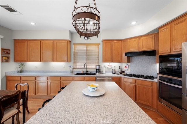 kitchen with visible vents, under cabinet range hood, light wood-type flooring, black appliances, and a sink