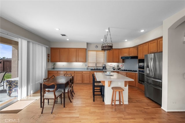 kitchen with under cabinet range hood, a breakfast bar, a sink, light countertops, and black appliances