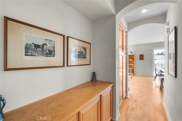 corridor featuring arched walkways, baseboards, and light wood-style floors