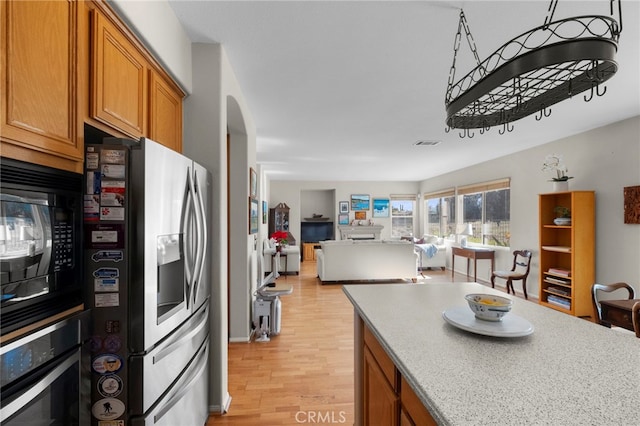 kitchen featuring brown cabinets, open floor plan, stainless steel fridge, black microwave, and oven