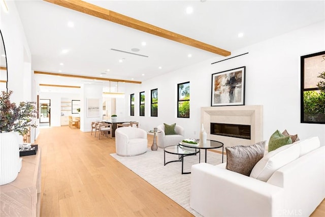 living room with beam ceiling, a premium fireplace, and light wood-type flooring