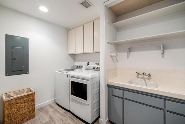 washroom featuring light wood-type flooring, washing machine and dryer, cabinets, electric panel, and sink