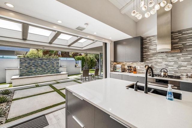 kitchen featuring pendant lighting, decorative backsplash, sink, stainless steel gas cooktop, and ventilation hood