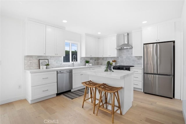 kitchen with appliances with stainless steel finishes, white cabinets, a kitchen bar, wall chimney range hood, and a kitchen island