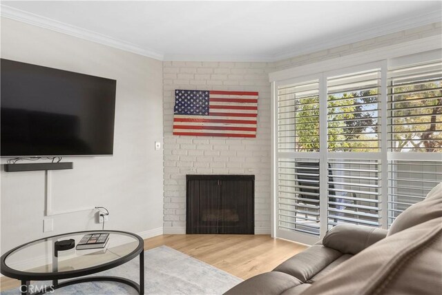 living room featuring a brick fireplace, wood-type flooring, and crown molding