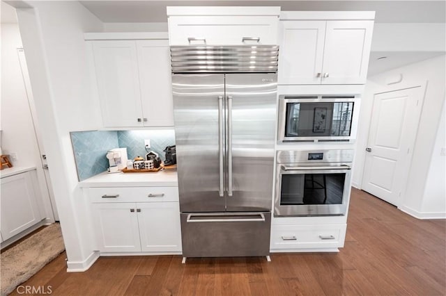 kitchen featuring hardwood / wood-style flooring, white cabinetry, tasteful backsplash, and built in appliances