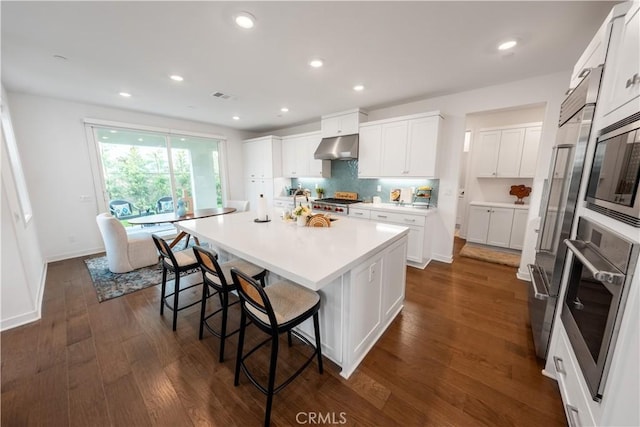 kitchen with white cabinets, appliances with stainless steel finishes, exhaust hood, dark wood-type flooring, and an island with sink