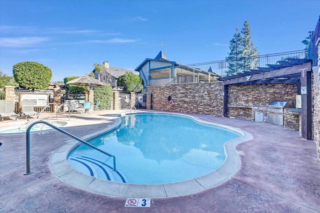 view of swimming pool featuring an outdoor kitchen, area for grilling, a pergola, and a patio