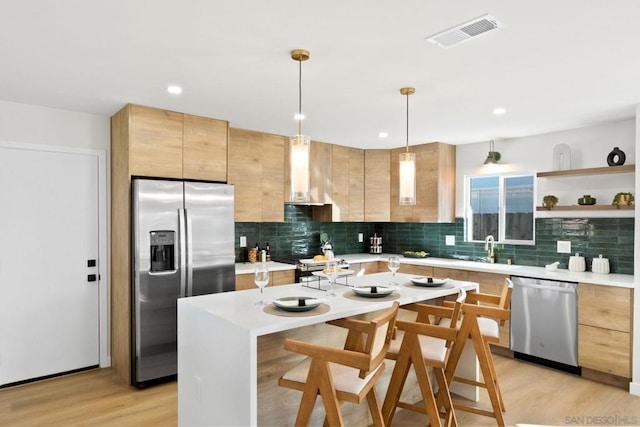 kitchen featuring decorative light fixtures, wall chimney range hood, a kitchen island, light hardwood / wood-style flooring, and stainless steel appliances