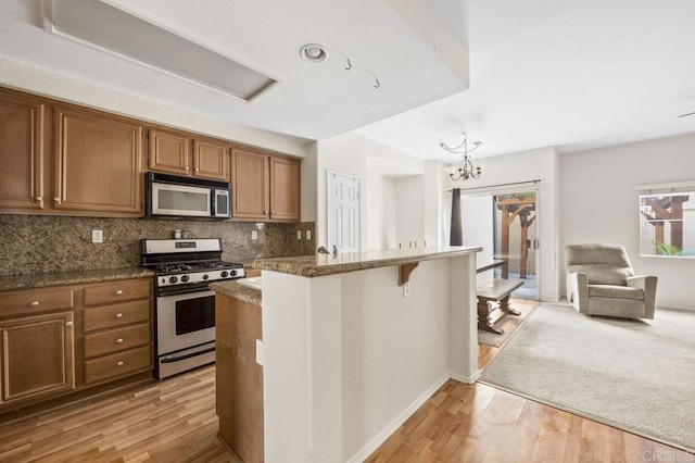 kitchen featuring light hardwood / wood-style floors, a kitchen bar, appliances with stainless steel finishes, decorative backsplash, and a chandelier