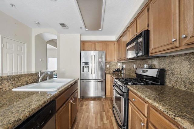 kitchen featuring stainless steel appliances, decorative backsplash, sink, stone countertops, and light wood-type flooring