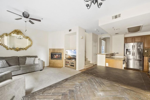 unfurnished living room featuring ceiling fan, sink, dark parquet flooring, and a tile fireplace