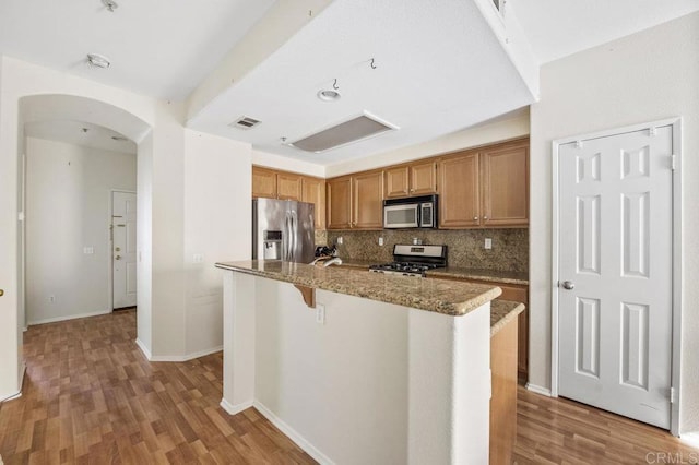 kitchen featuring backsplash, a center island, a kitchen bar, appliances with stainless steel finishes, and light stone counters