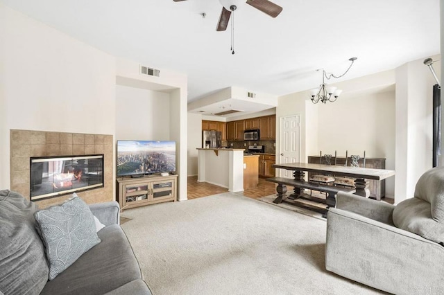 living room with ceiling fan with notable chandelier, light colored carpet, and a tile fireplace