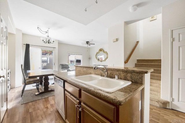 kitchen featuring ceiling fan with notable chandelier, light hardwood / wood-style floors, sink, stainless steel dishwasher, and a center island with sink