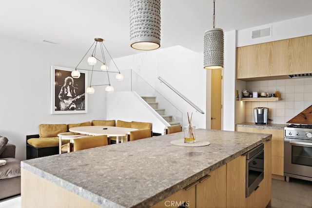 kitchen featuring a kitchen island, decorative backsplash, hanging light fixtures, built in microwave, and stainless steel gas stove