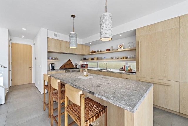 kitchen featuring light brown cabinets, a kitchen breakfast bar, hanging light fixtures, light stone counters, and a center island