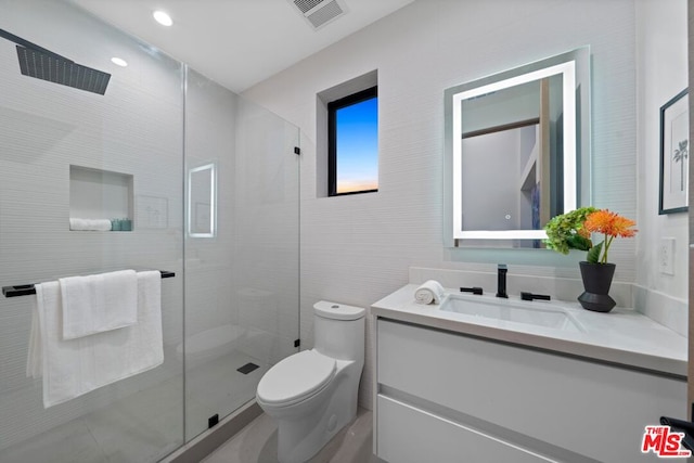 bathroom with toilet, tile walls, a shower with shower door, and vanity