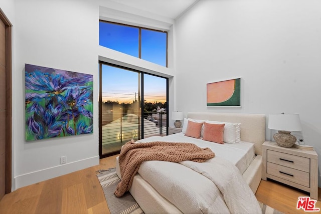 bedroom featuring access to exterior, light hardwood / wood-style floors, and a high ceiling