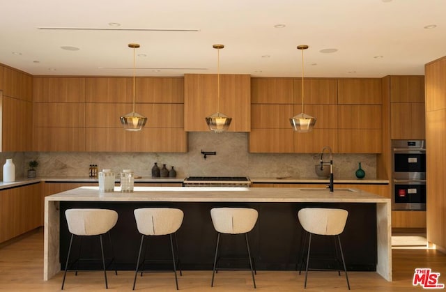 kitchen with a breakfast bar area, decorative light fixtures, stainless steel double oven, and a kitchen island with sink