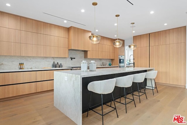 kitchen featuring decorative light fixtures, light brown cabinets, a large island, oven, and light wood-type flooring