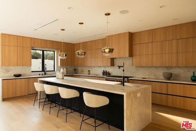 kitchen featuring pendant lighting, a kitchen bar, decorative backsplash, light wood-type flooring, and a center island with sink